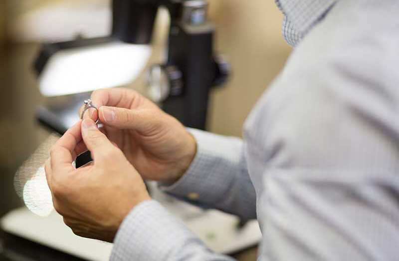 A Conrad jeweler examining a diamond ring up close at the bench